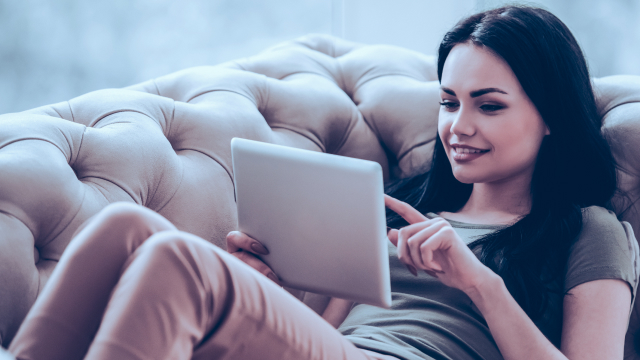 A woman relaxing on a couch buying a digital product on her tablet